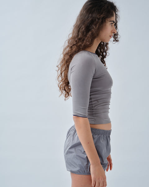 Side of woman wearing grey 3/4 sleeve ribbed top with grey check shorts