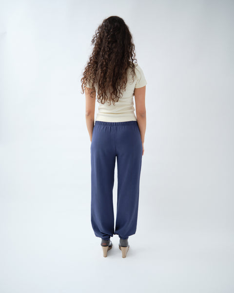 Back of woman wearing yellow v-neck tshirt, with navy trousers & grey socks