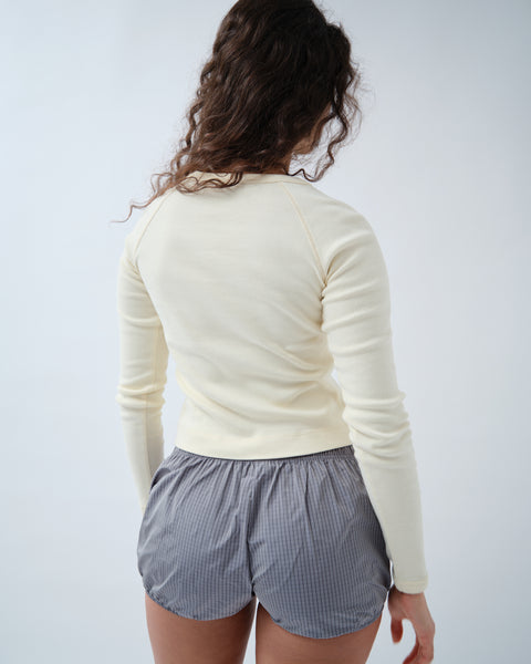 Back of woman wearing yellow long sleeve top and grey check shorts