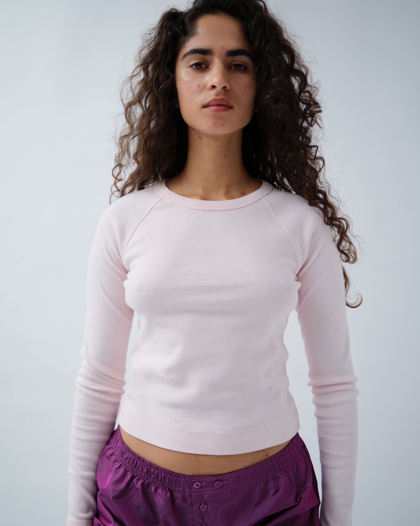 Front of woman wearing light pink long sleeve tshirt with purple shorts