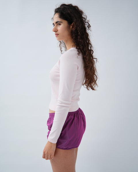 Side image of woman wearing pink long sleeve tshirt and purple shorts