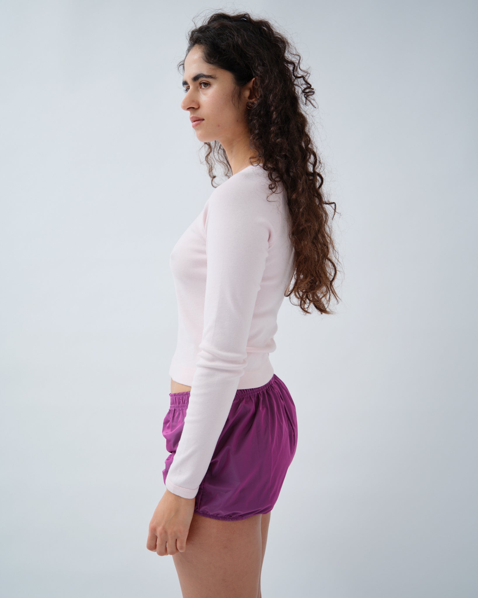 Side of woman wearing light pink long sleeve tshirt with purple shorts